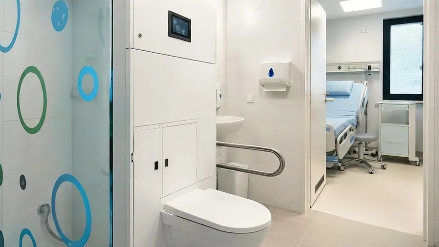 Patientenbad in der Nuklearmedizin mit Wand-WC und einem Krankenhausbett im Hintergrund